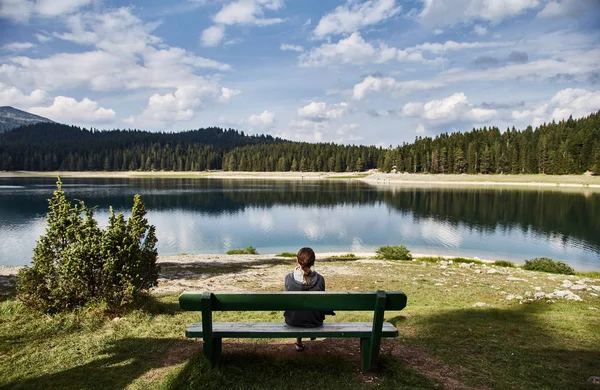 Młoda dziewczyna siedzi na ławce. Czarne jezioro. Park Narodowy Durmitor. Czarnogóra. — Zdjęcie stockowe