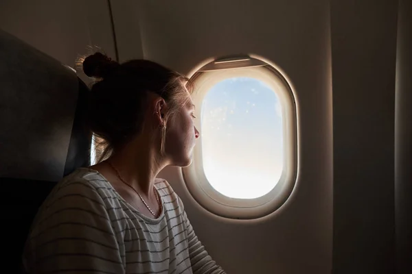 Meisjes kijkt uit het raam van het vliegtuig. — Stockfoto