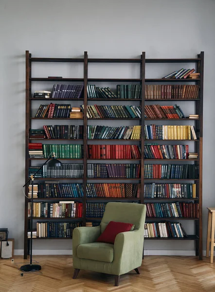 Зелене крісло в інтер'єрі. Книжкова шафа зі старими книгами на полицях. Книги в старому дерев'яному шафі — стокове фото