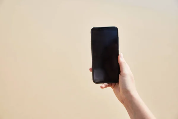 Mobile phone in female hand on the background of the beach and ocean — Stock Photo, Image