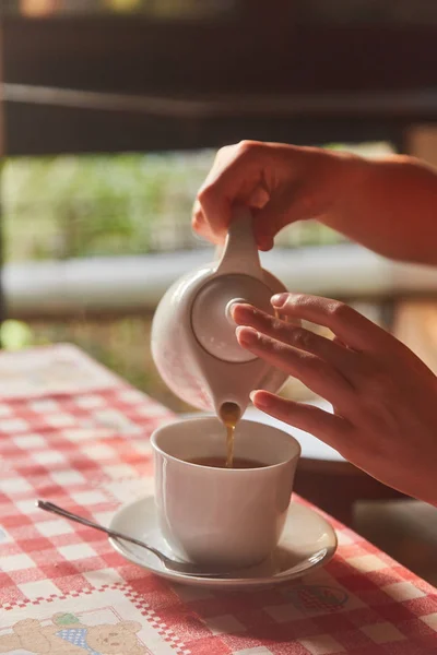 Girl pours tea in a cup. Cup of tea on the table. A Cup of freshly brewed black tea,escaping steam,warm soft light