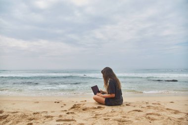 Sahilde bilgisayarda çalışan genç kız. Sahilde çalışma serbest meslek.
