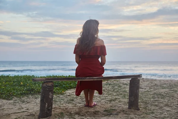 Chica joven sentada en un banco en el océano — Foto de Stock
