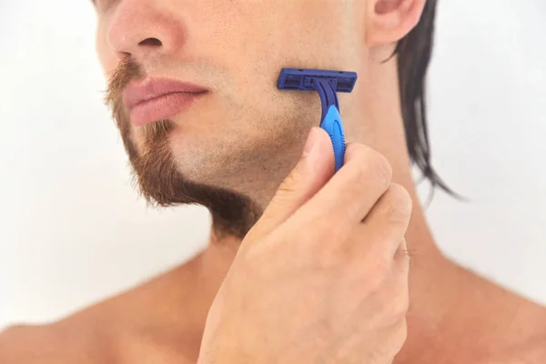 Medio afeitado. Un joven con barba en la mitad de la cara sobre fondo gris claro . — Foto de Stock
