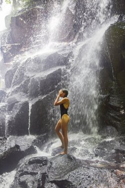 Genç bir kız şelalenin altında duruyor.