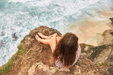 Genç bir kız uçurumda oturuyor. Bali, Uluwatu. 