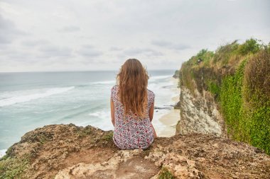 Genç bir kız uçurumda oturuyor. Bali, Uluwatu. 