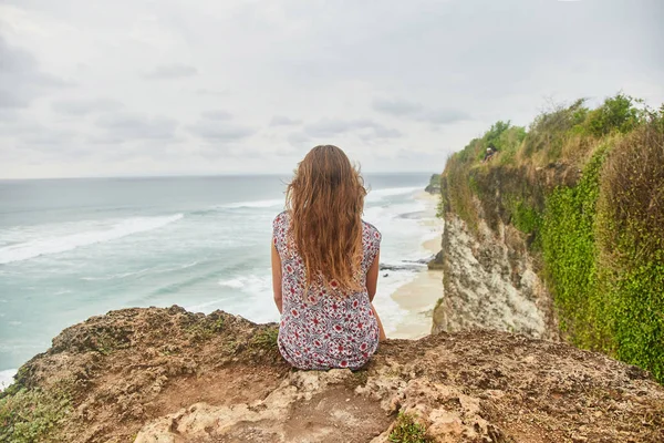 Una joven está sentada en un acantilado. Bali, Uluwatu . — Foto de Stock