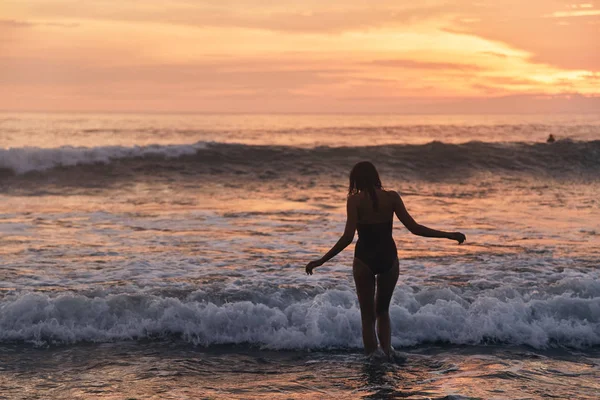 Hermoso atardecer. Silueta de mujer joven caminando en la playa del océano . — Foto de Stock