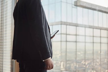 Ofisinde kalırken akıllı telefon kullanarak siyah takım elbiseli genç işadamı yakın.