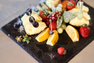 Meyve şık bir tabakta dilimlenmiş. Ananas, armut, portakal, elma, üzüm, yabani çilek.