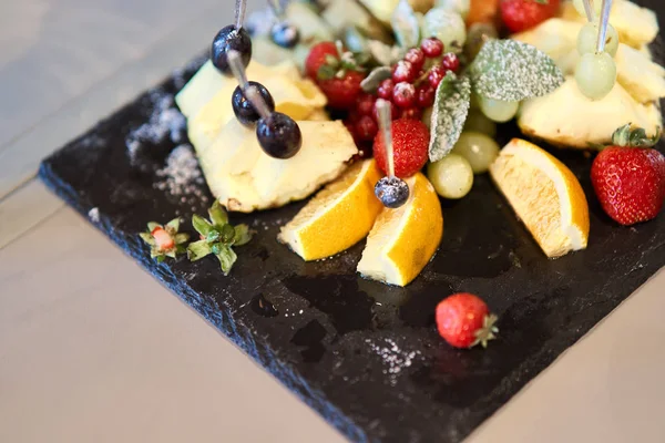 Plody nakrájené na stylové desce. Ananas, hrušeň, pomeranč, jablíčko, hrozen, jahodový. — Stock fotografie