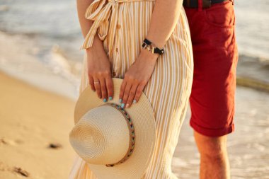 Bir kızın elinde hasır bir şapka. Sahil boyunca yürüyün