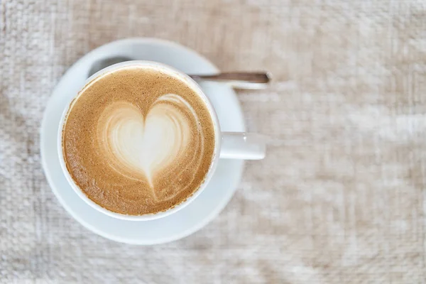 Vista superior de una taza con café con leche sobre un fondo marrón. Café con forma de corazón — Foto de Stock