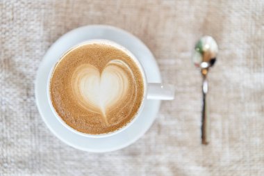 Kahverengi bir arka plan üzerinde latte ile bir kupa üst görünümü. Kalp şeklinde kahve