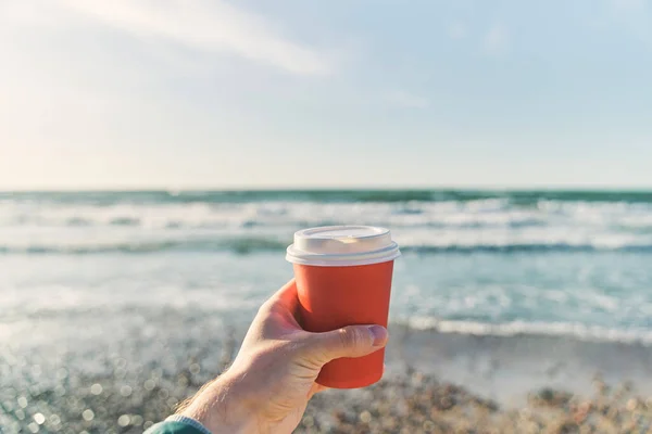 한 젊은이 가 바다 뒤에 커피를 담은 종 이 잔을 들고 있다 — 스톡 사진