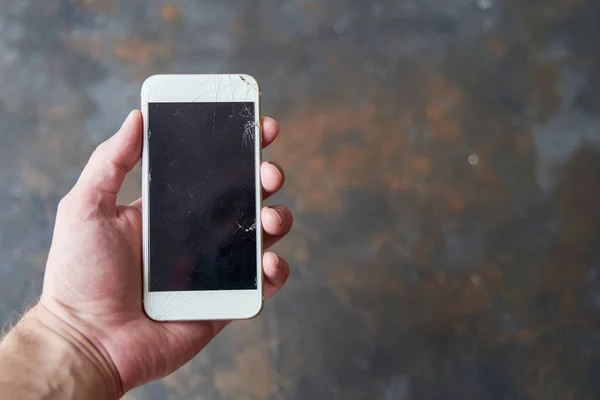 A young man holds a smartphone with a broken screen in his hand on a dark background. Mockup — Stock Photo, Image