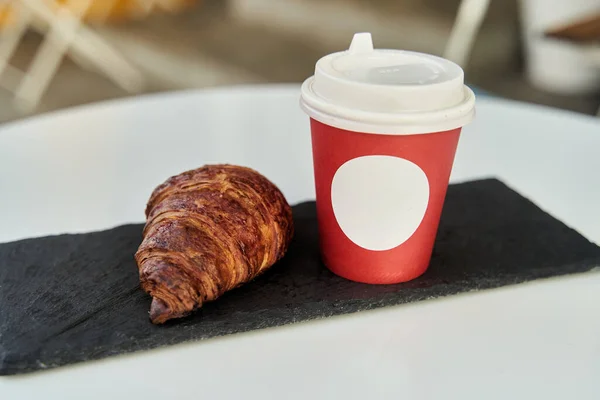 कॉफीसह लाल कप आणि कॅफेमध्ये टेबलवर एक क्रॉझंट . — स्टॉक फोटो, इमेज