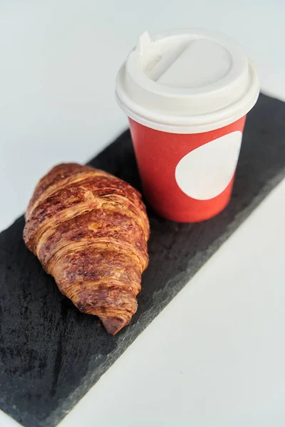 Red cup with coffee and a croissant on a table in a cafe. — Stock Photo, Image