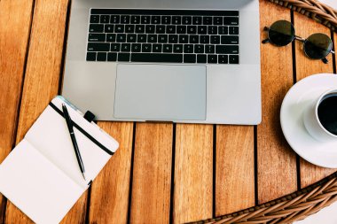 Dizüstü bilgisayarda çalışmak için çalışma alanı, kahverengi ahşap masa, bir fincan kahve ve kayıt defterleri. Serbest meslek kavramı. Uzaktan kumanda. Yer kopyala