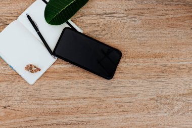 Düz yatış, beyaz kağıt ve kalem ile bir not defteri üst görünüm yaklaşan bir gezi planlamak için, ya da serbest plan. Güzergahı görmek için akıllı telefon. Not defterinde deniz kabukları ve yakınlardaki tropikal çarşaflar. Seyahat konsepti. Metin veya resim için yer, kopyalama yeri