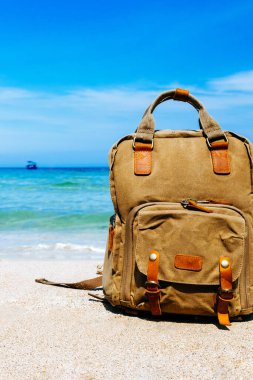 Seyahat, tatil boyunca tropik bir plajın kıyısında turist tarzı kahverengi sırt çantası. Kumsal, arka planda deniz manzarası. Serbest çalışan sırt çantası. Yer kopyala