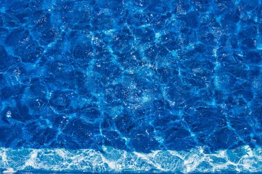 Yüzme havuzu, açık havuzda mavi berrak su, yüzeyinde güneş parlaması. Havuzdaki mavi suyun arka planı. Suyun yüzeyinde dalgalanmalar. Yer kopyala