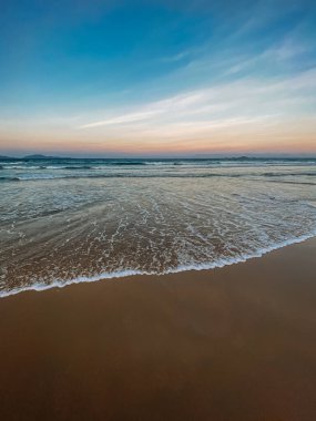 Denizde dalgalar, gelgit, kumlu sahil, köpük. Beyaz bulutlu açık mavi gökyüzü. Seyahat konsepti, yaz tatili. Asya 'da seyahat. Denizde gün batımı, renkli gökyüzü. Yer kopyala