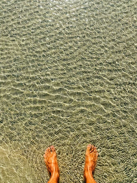 澄んだ海の男の足 海の透明な水の上に小さな波 晴れた日には水の表面に太陽のまぶしさ 穏やかな海の波の背景 スペースのコピー — ストック写真