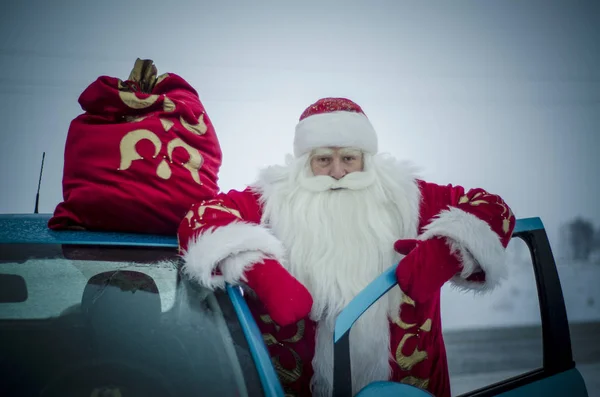 圣诞老人站在蓝色的车旁边带着一袋礼物 — 图库照片