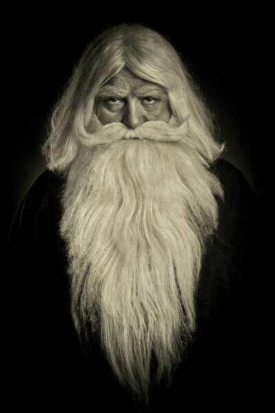 The patriarchal religious elder with a long gray beard sternly looks at the dark background in sepia