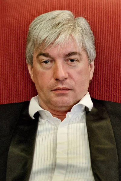 A grey-haired elderly man sitting in a red armchair. A grey-haired elderly imposing man sitting in a red armchair and looking sadly.