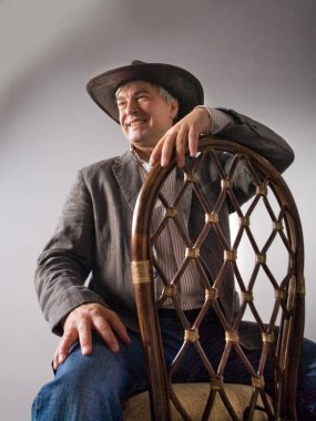 Saygın bir gri saçlı Latin erkek şapka içinde. Saygın bir gri saçlı Latin erkek şapka ve bir ceket bir kovboy gibi bir antika hasır sandalyede oturuyor.