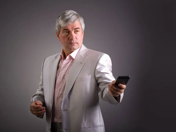 Animposing respectable grey-haired man. A handsome imposing respectable grey-haired man wearing a light-colored jacketis holding a mobile phone.