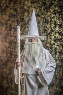 Beyaz bir pelerin ve bir kap koyu altın dokulu bir arka plan karşı bir kadro ile gri saçlı sakallı şiddetli Sihirbazı.