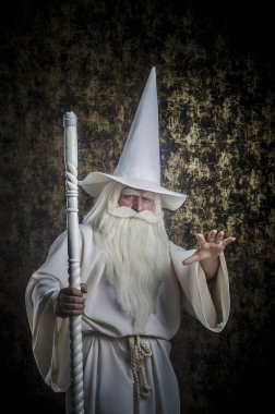 Beyaz bir pelerin ve bir kap koyu altın dokulu bir arka plan karşı bir kadro ile gri saçlı sakallı şiddetli Sihirbazı.