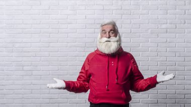 Noel Baba'nın resimdeki kırmızı ceket gri saçlı sakallı adam beyaz bir duvar karşı ayakta ve duygusal olarak poz.