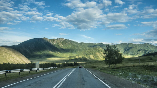 Beautiful views and landscape of Altai nature. Perspective of the road and highway in Altai, against the backdrop of majestic mountains covered with forest and sky with clouds.