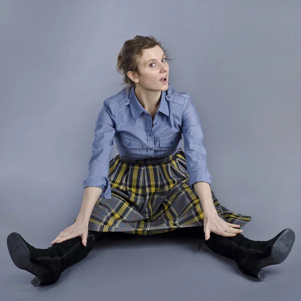 A beautiful European woman is funny and originally sits on the floor. A beautiful European woman is funny and originally sits on the floor in a blue shirt and a checkered skirt on a blue background.