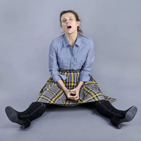 A beautiful European woman is funny and originally sits on the floor. A beautiful European woman is funny and originally sits on the floor in a blue shirt and a checkered skirt on a blue background.