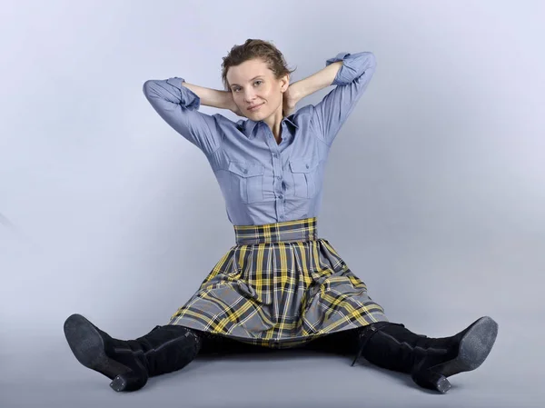 A beautiful European woman is funny and originally sits on the floor. A beautiful European woman is funny and originally sits on the floor in a blue shirt and a checkered skirt on a blue background.