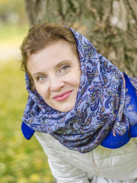 Beautiful European woman in autumn park. Beautiful European smiling woman in a blue scarf in the autumn park.