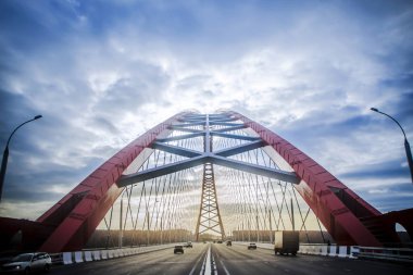 Beautiful background and view, landscape and panorama of the modern cable-stayed arched type, the red bridge and the road with cars against the blue sky with clouds. clipart