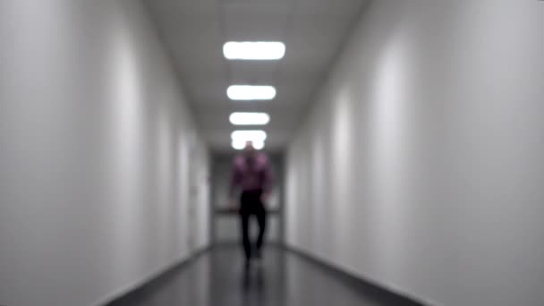Satu orang berjalan menyusuri koridor putih yang panjang. Latar belakang kabur. Video berisi flicker dan noise — Stok Video
