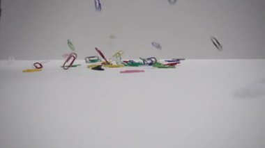 Beyaz arkaplanda izole edilmiş renkli ataçlar. Çok renkli klipsler masaya düşer. Slow Motion 250 fps. Ofis kavramı.