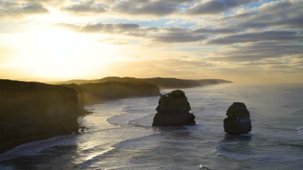 日出通过云彩十二使徒海洋国家公园海岸线以海浪在近海海堆栈附近维多利亚澳洲 — 图库视频影像