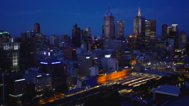 オーストラリア ビクトリア州メルボルン オーストラリア 2018 乗客と照らされたフリンダース ストリート駅のプラットホーム メルボルン Cbd 商業高層ビルの夜景を訓練します — ストック動画