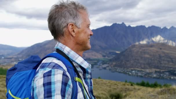 幸せな引退した白人男リマーカブルズ湖ワカティプ新しいニュージーランドのトレッキングを楽しんでいる双眼鏡でカジュアルな服を着て — ストック動画