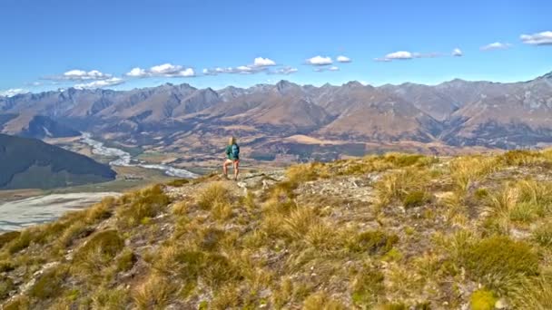 ニュージーランドの南の島の風景の中のハイキングを楽しむリュックサックと若いアクティブな白人女性ハイカーの空中ドローン — ストック動画