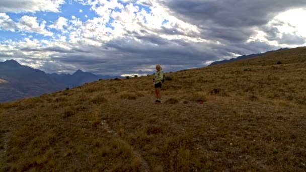 空中ドローンのバックパックを退職 リマーカブルズ湖ワカティプ オタゴ ニュージーランド ハイキングを楽しむアクティブな白人の年配の女性の — ストック動画